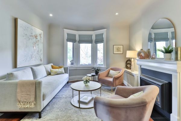 Elegant living room with automated shades in bay window, fireplace, mirror, and blush accent chairs.