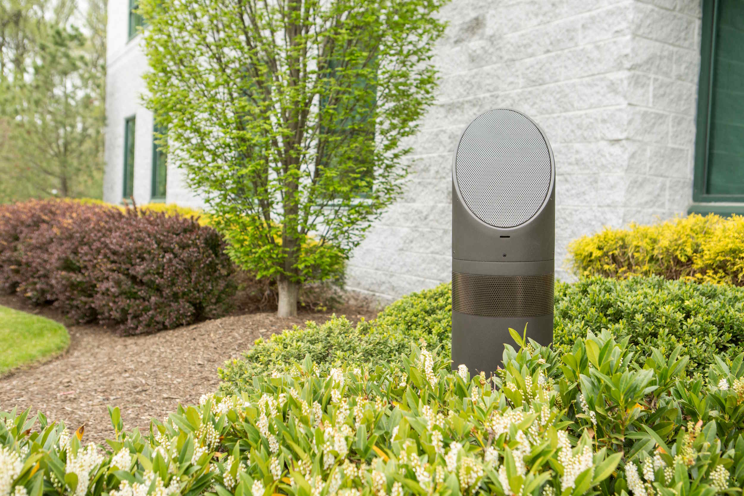 Freestanding outdoor landscape speaker discreetly installed among garden shrubs and flowering plants for whole-yard audio.