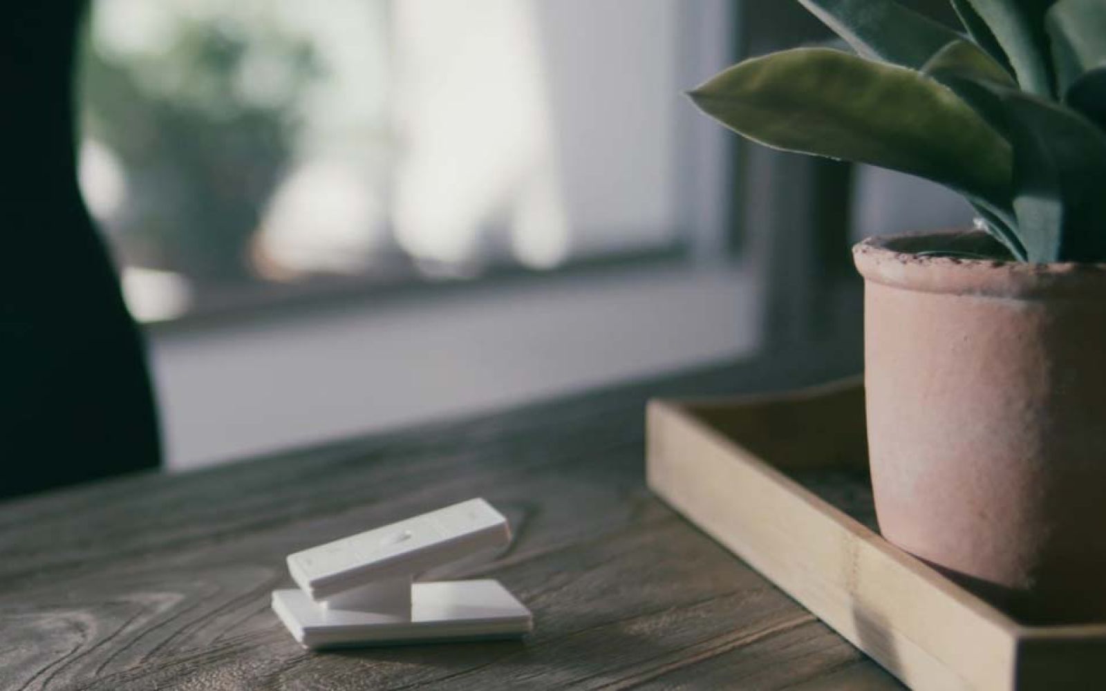 Stack of white smart remotes on wooden table next to potted plant