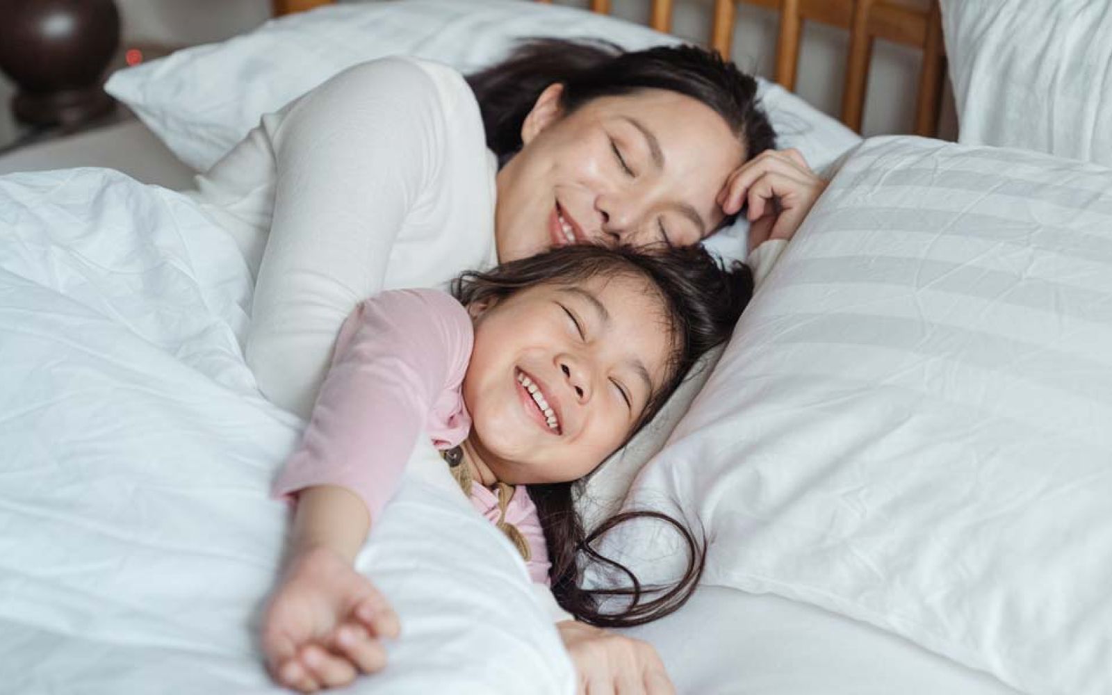 Woman smiling while sleeping next to child in bed