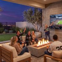 Patio with fire pit and wall-mounted TV showing a football game, friends in jerseys cheer together at dusk