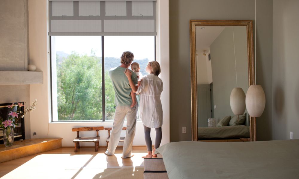 <span class="uk-h4">A young couple stands with their baby looking out a large picture window.</span>